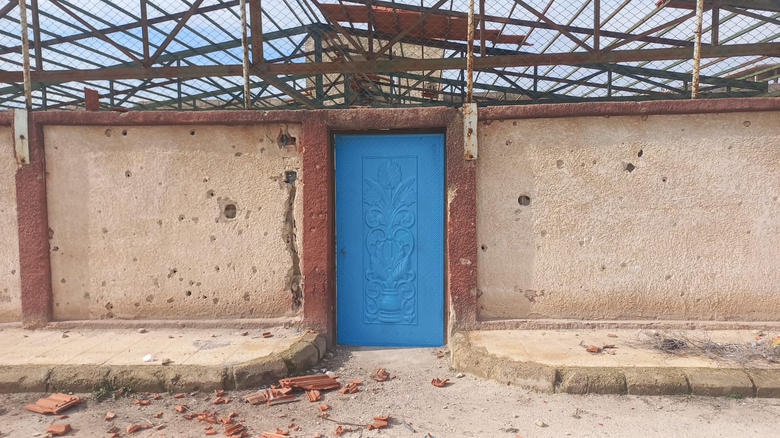 Frisch blau lackierte Eingangstür in einer von Einschusslöchern gezeichneten Mauer